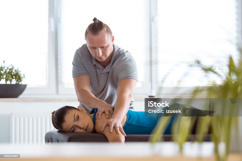 Physiotherapist massaging young woman's back Massage therapist giving shoulder massage to young woman. Patient lying on massage table. Chiropractic Adjustment Stock Photo