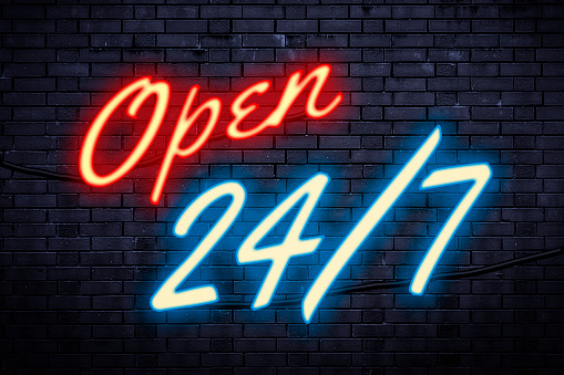 Service open any time and every day or operating nonstop concept theme with a red and blue light neon sign against a brick wall with the text Open 24/7