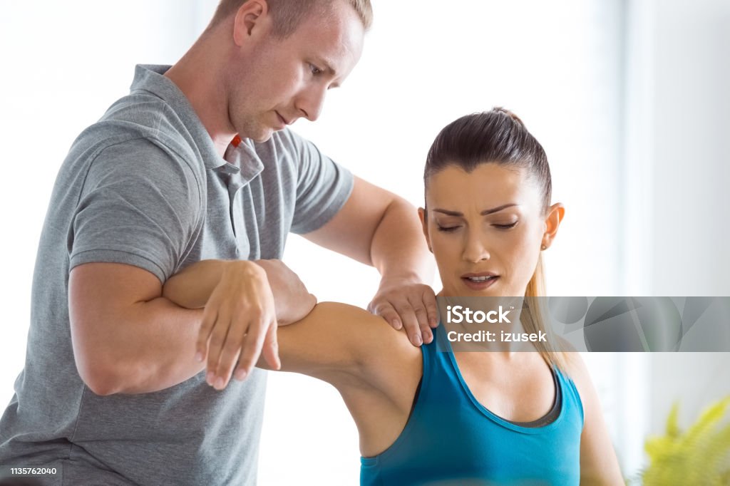 Physiotherapist massaging young woman's shoulder Physical therapist giving shoulder massage to young woman in his office. Close up of patient. Back Stock Photo
