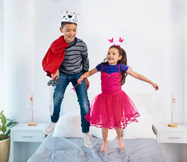 Shot of two young children dressed up as superheroes jumping on a bed at home