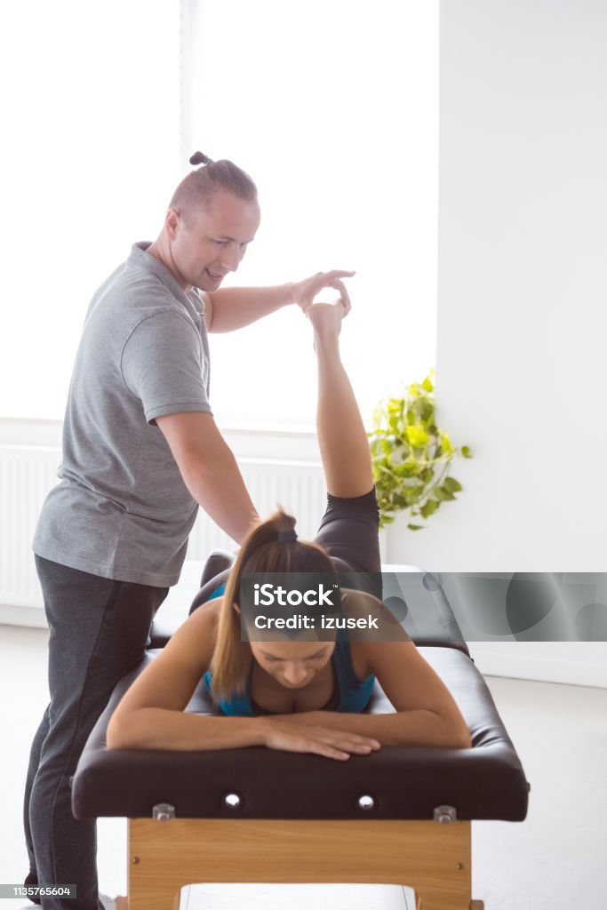 Massage therapist stretching young woman's legs Physical therapist giving legs massage to young woman in his office. Patient lying on massage table. Adult Stock Photo