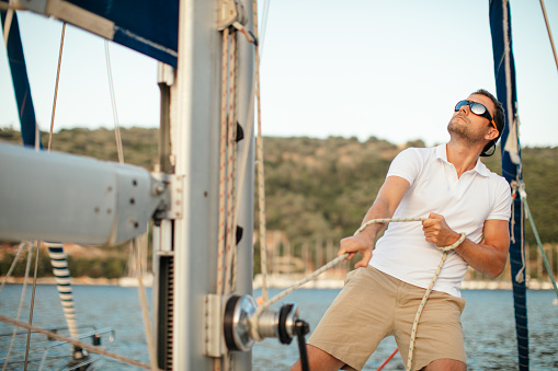 Handsome mid adult skipper on sailboat pulling rope and adjusting sails and ropes while out of sailing