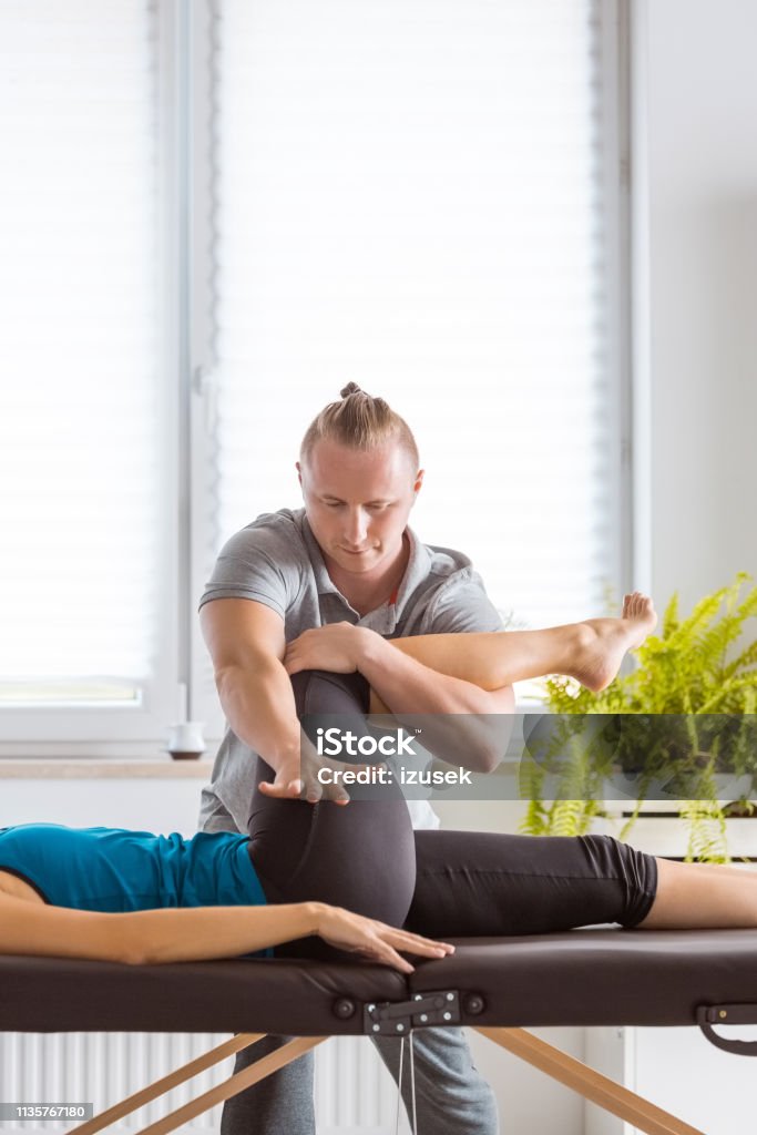Physiotherapist massaging young woman's legs Physical therapist giving legs massage to young woman in his office. Patient lying on massage table. Hip - Body Part Stock Photo