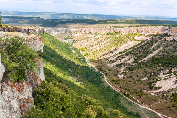 istock A deep canyon, a ravine covered with vegetation, grass, shrubs and trees, on the bottom of which is laid a dirt road to the village located in it 1135768633