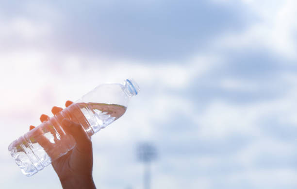 istock Woman hand holding a drinking water bottle on blue sky background with sunlight. Cool drinking water. World Water Day concept. 1135771518
