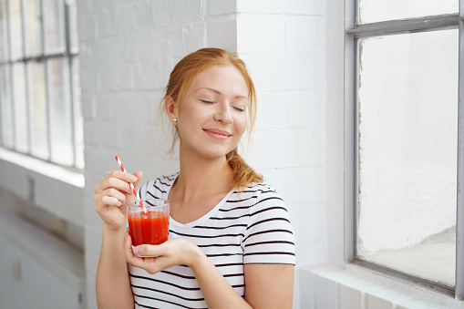 Pretty young red head enjoys her tomato based beverage and the warm afternoon sun streaming in through a nearby window