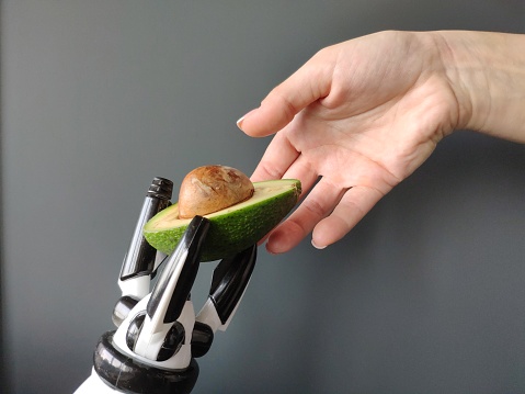 A robot's hand stretches an avocado into a woman's hand, background or concept, free space for text.