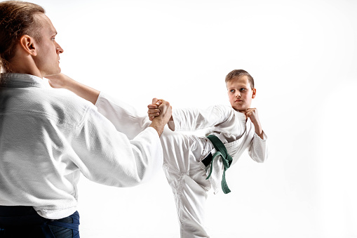 Man and teen boy fighting at Aikido training in martial arts school. Healthy lifestyle and sports concept. Fightrers in white kimono on white background. Karate men with concentrated faces in uniform.