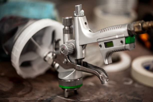 A close-up of a paint spray gun laid on it's front part on the table in a workshop.