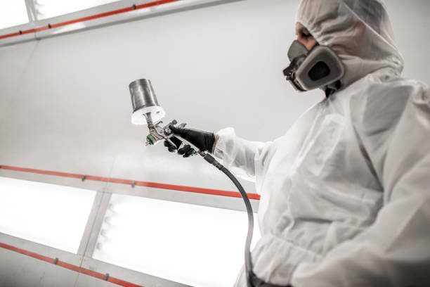 istock Car painter in white coveralls and a breathing mask purging a paint spray gun before work in a painting chamber 1135775917