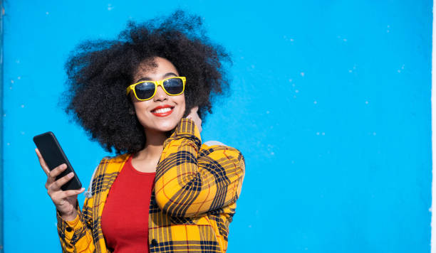Smiling american-african woman using smart phone on a blue background