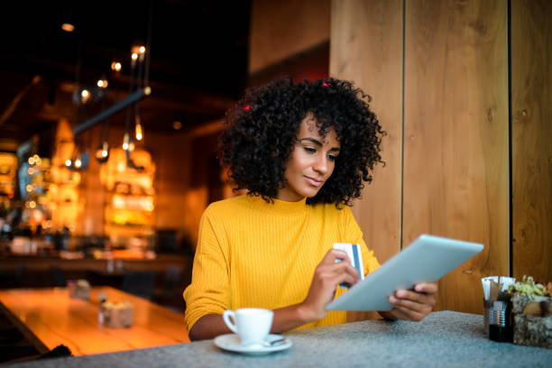 Electronic banking. Beautiful smiling African American woman using digital tablet at the bar. credit card purchase stock pictures, royalty-free photos & images