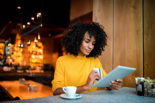 Beautiful smiling African American woman using digital tablet at the bar.