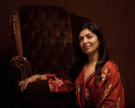 Portrait of a mid adult woman, looking at the camera while posing and resting on an arm chair.