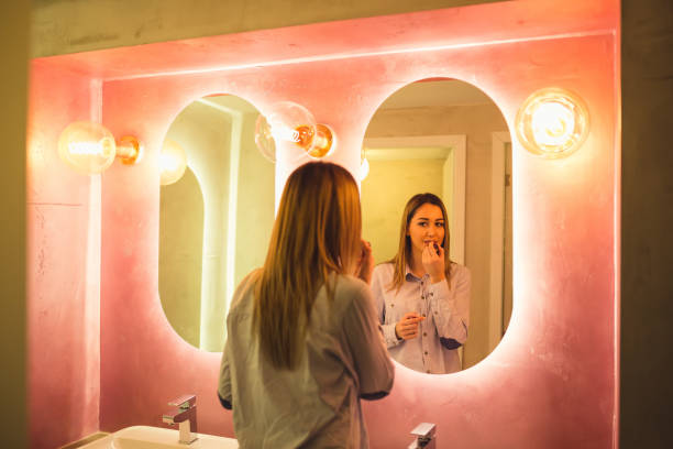 Attractive happy woman applying makeup in the bathroom of a restaurant The woman paints lips in the toilet. Attractive happy woman applying makeup in the bathroom of a restaurant - Image restaurant mirror stock pictures, royalty-free photos & images