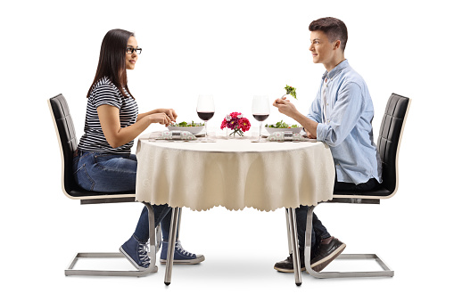 Full length profile of a young male and female eating a salad in a restaurant isolated on white background