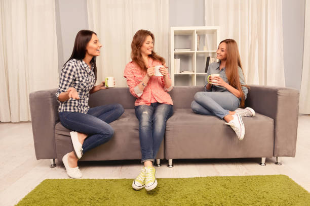 istock Attractive sisters sitting on couch and having talk with coffee 1135780538