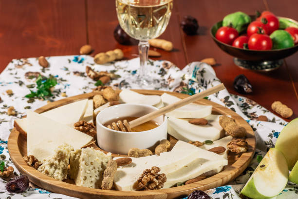 istock Assorted cheeses on round wooden board plate served with white wine Guda cheese, cheese grated bark of oak, hard cheese slices, walnuts, grapes, crackers, honey, sulguni, light wood background 1135782332