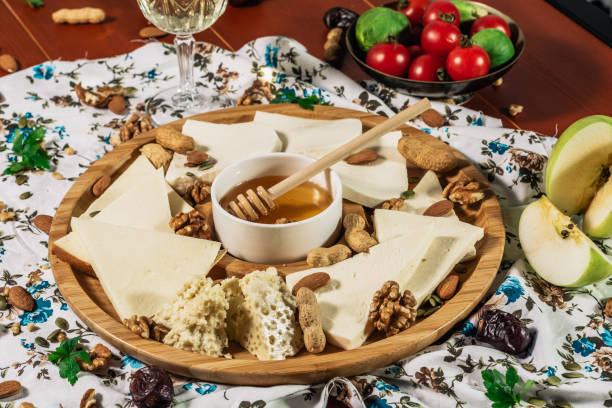 istock Assorted cheeses on round wooden board plate served with white wine Guda cheese, cheese grated bark of oak, hard cheese slices, walnuts, grapes, crackers, honey, sulguni, light wood background 1135782486