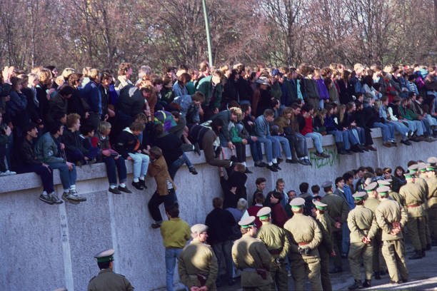 Berlin, Germany- November 10, 1989: These pictures is taken at the „Pariser Platz“ where the Brandenburger gate is located in the center of Berlin near the Reichstag building. It is the next morning after the fall of the Berliner wall. You can see people who have climbed the wall from the west side of the city and are now sitting or standing on the wall which separated west from east Berlin for the last 28 years. They would like to jump down to walk under the Brandenburger Gate to the east side of Berlin. But on the east side of the wall the national police force of the German Democratic Republic is standing peacely in a row in order to avoid that people cross the boarder. Two days ago these image woud not have been possible, the national national police force of the German Democratic Republic had the order to kill anybody trying to cross the boarder. \