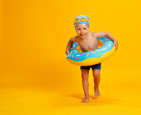 happy child boy in swimsuit with swimming ring donut on colored yellow background