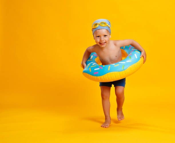 happy child boy in swimsuit with swimming ring donut on colored yellow background happy child boy in swimsuit with swimming ring donut on a colored yellow background inflatable photos stock pictures, royalty-free photos & images