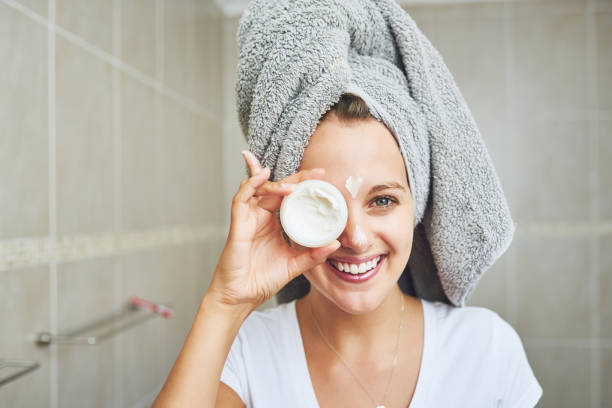 Here's a little beauty tip Portrait of an attractive young woman applying moisturizer to her face at home woman wrapped in bath towel stock pictures, royalty-free photos & images