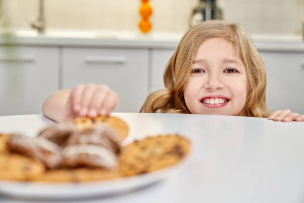 istock Child hiding and taking biscuits with raisins from table. 1135789224