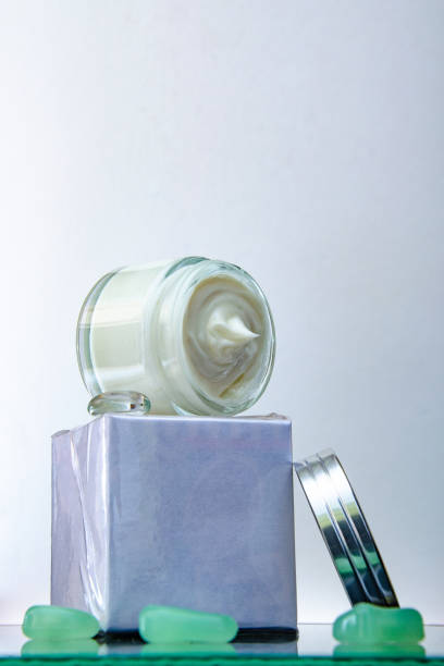 istock open jar of cream, a box, and colored pebbles on a glass table. White background. 1135790002