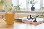 istock Yellow cup of tea, book and glasses on the table, cozy home interior background 1135791694