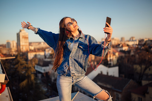 Young woman on the rooftop, taking a selfie during sunset