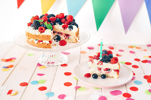 Berry birthday cake with colourful confetti and bunting on white wooden table