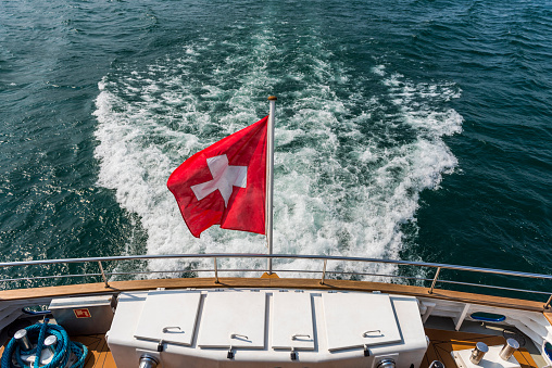 Wake and Swiss flag swaying in the wind on ship, Geneva, Switzerland