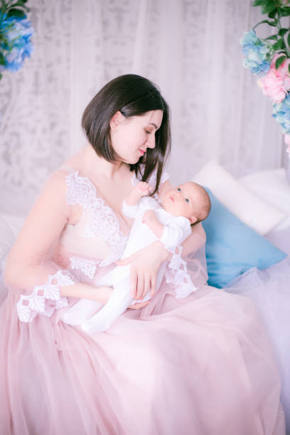 Young mother in a boudoir dress with a baby in her arms in spring flowers stock photo