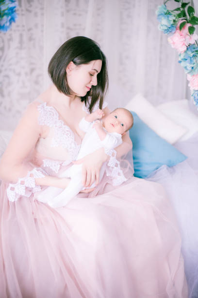 Young mother in a boudoir dress with a baby in her arms in spring flowers stock photo