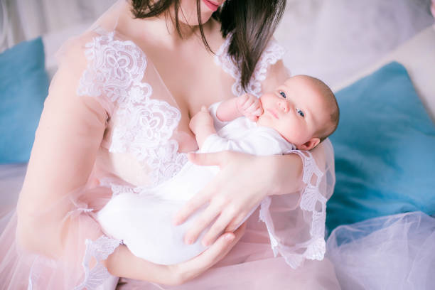 Young mother in a boudoir dress with a baby in her arms in spring flowers stock photo