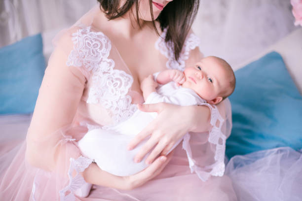 Young mother in a boudoir dress with a baby in her arms in spring flowers stock photo