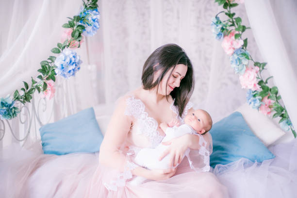 Young mother in a boudoir dress with a baby in her arms in spring flowers stock photo