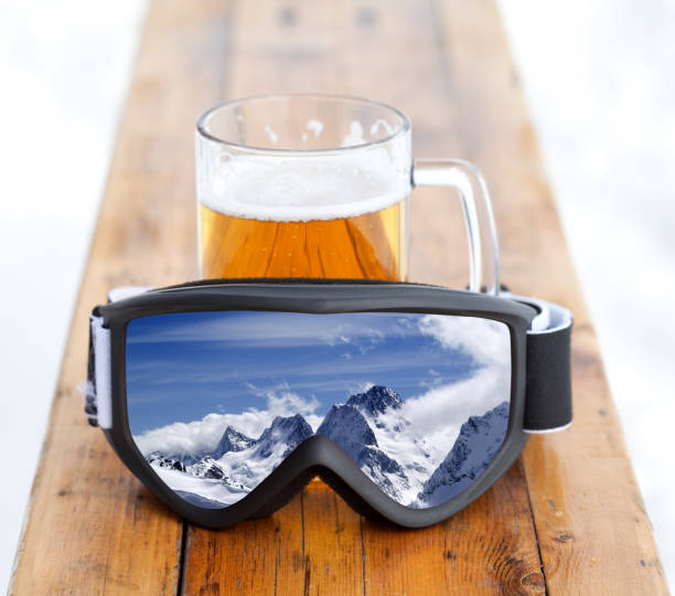 óculos de proteção do esqui com reflexão das montanhas e da caneca de vidro com cerveja fria fresca - atividades depois de esquiar - fotografias e filmes do acervo