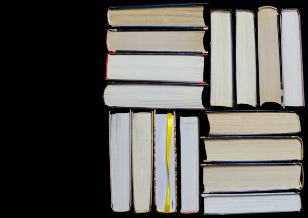istock Many multicolored thick open books stand on a dark background. On the books are old round glasses and an open notebook with a pencil. 1135807029