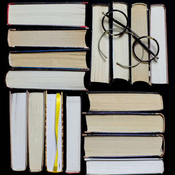 istock Many multicolored thick open books stand on a dark background. On the books are old round glasses and an open notebook with a pencil. 1135807038