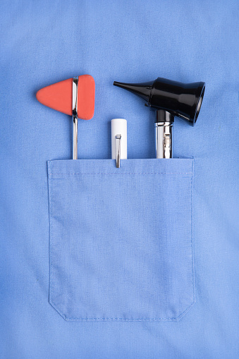 The pocket of a doctor's scrubs containing an otoscope, flashlight and reflex hammer.