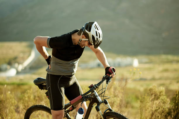 I'm spending more time on my warmup next time Shot of a mature man experiencing back pain while out for a ride on his mountain bike backache photos stock pictures, royalty-free photos & images