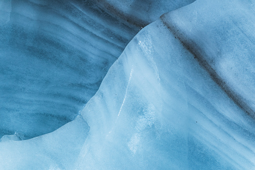 Close-up wall of a centuries-old glacier with a structure of stripes and bubbles. Ice blue light texture.