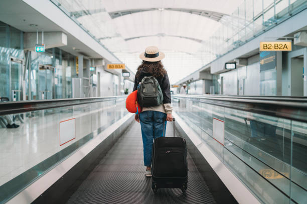 молодая женщина в аэропорту с чемоданом - борт отъезда прибытия стоковые фото и изображения