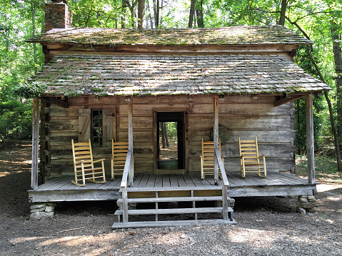Empty wooden rocking chairs on the front porch of an old log house in the woods. This log house was built in the pioneer days of America during the 1830s.