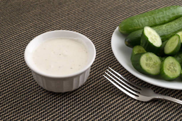 Sliced and whole cucumbers with ranch dressing A small bowl of ranch dressing with sliced and whole bite size cucumbers on a white plate plus a fork in the foreground on a tablecloth. ranch dressing stock pictures, royalty-free photos & images