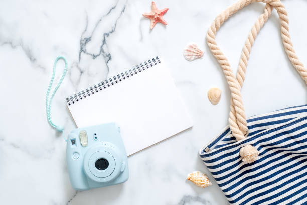 istock Summer travel composition on a marble background. Women's desk with instant photo camera, striped beach bag, seashells and blank notepad. Lifestyle of traveler, beauty blogger, digital nomad, hipster. 1135852011