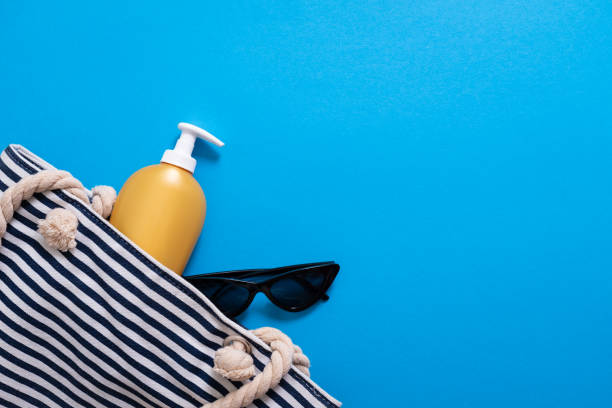 composição do verão. saco de praia despojado com creme de bronzeador e óculos escuros. conceito do feriado de verão, protetor solar cosmético e acessórios no fundo azul do mar. - bolsa de praia - fotografias e filmes do acervo