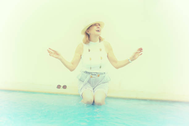 senior attivo: donna che spruzza sul bordo della piscina - women wading sun hat summer foto e immagini stock